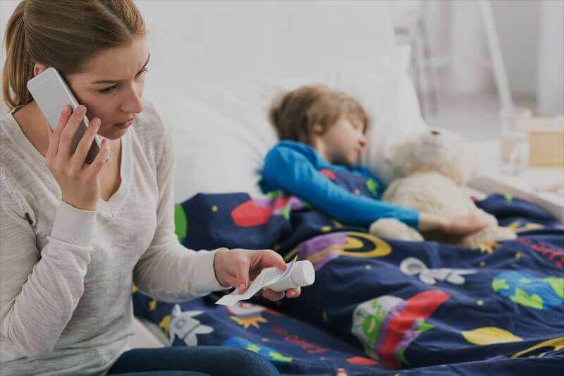 病気の子供の横で電話をかけている心配そうな母親