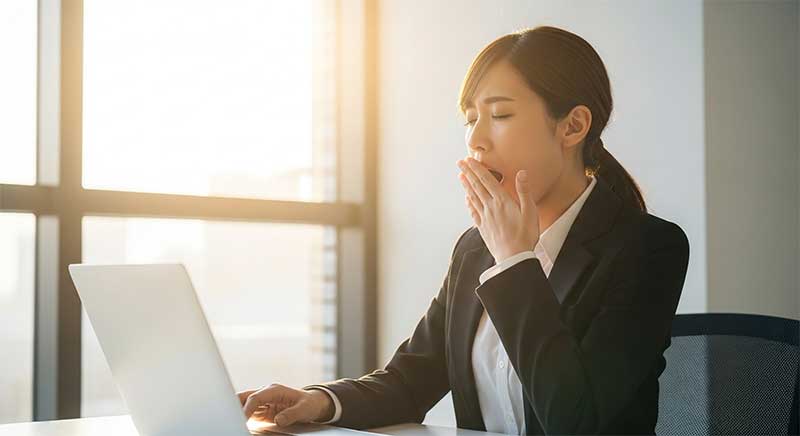 眠さをこらえて仕事している女性 ホメオパシーのレメディーをとって眠そうな女性