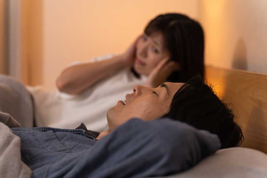 いびきをかく男性の横で妻がみみをふさいでいる